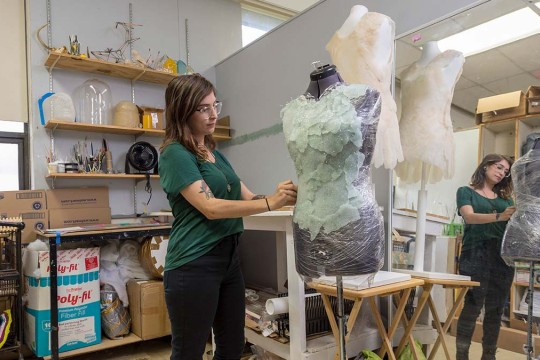 student adjusts a light green fabric on a mannequin.