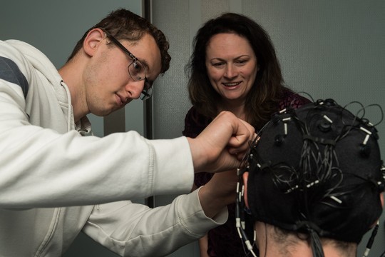 student researcher adjusts a cap with electrodes on a subject.