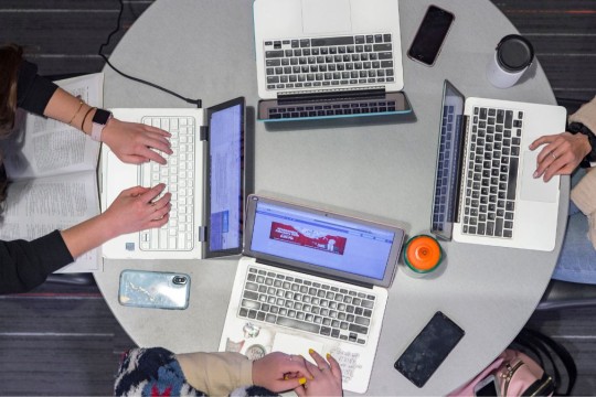 four students at a round table with laptops collaborating