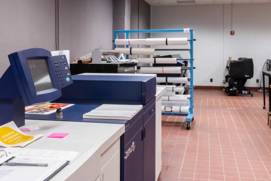 Printer with a rack of rolled paper in the background