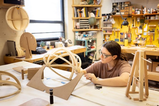 student works in a wood shop, forming a round frame.
