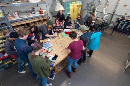 Group of students standing around a workbench painting props