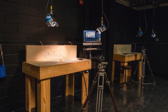 Stop motion film set in a black room with wooden stages and lights hanging from the ceiling