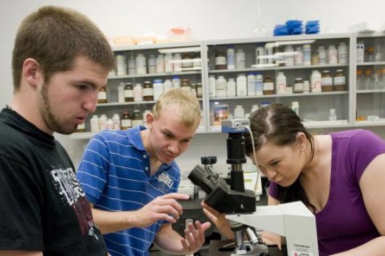 3 people adjusting a microscope in a lab