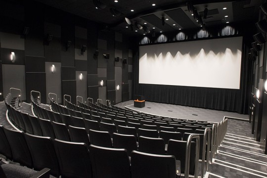 empty theater with stadium seating, stage, podium, and large screen.