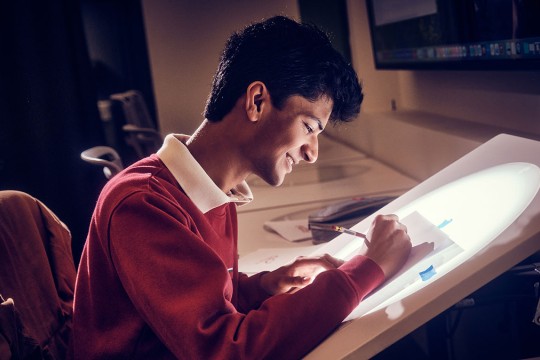 A smiling student draws on a light table.