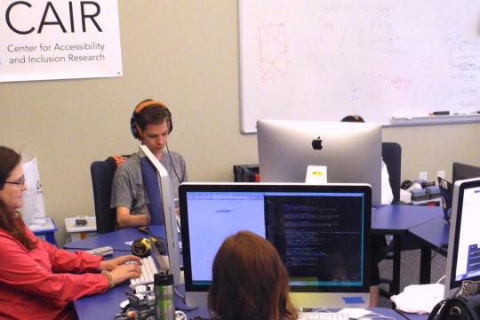 Students sitting around a desk, using computers.
