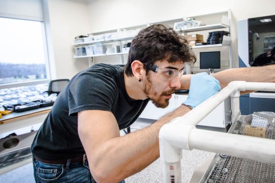 Man in goggles working on a plastic tube model design.