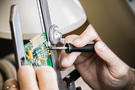 Electronic circuit board being repaired with tool.