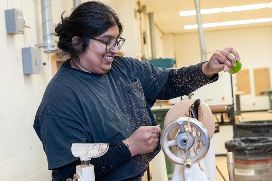 student smiles as she uses a lathe.