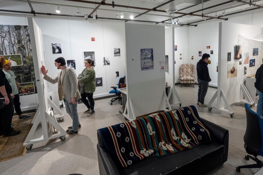 people walk through an art gallery space, with white walls and rolling dividers.