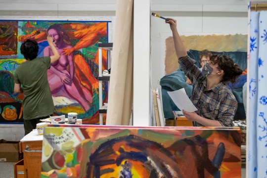 two students painting in a studio space, with one student's work depicting a nude woman in pinks and purples.
