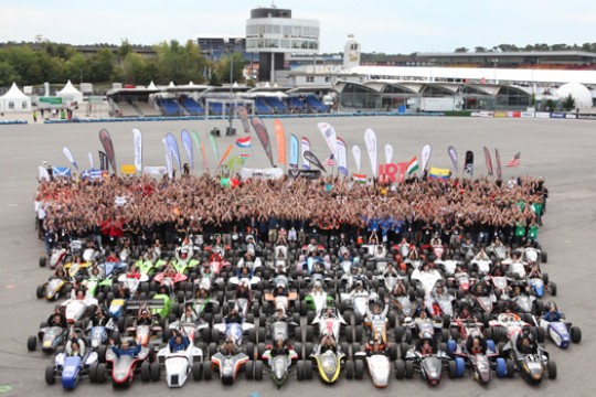 People and formula cars gathered on a race track.