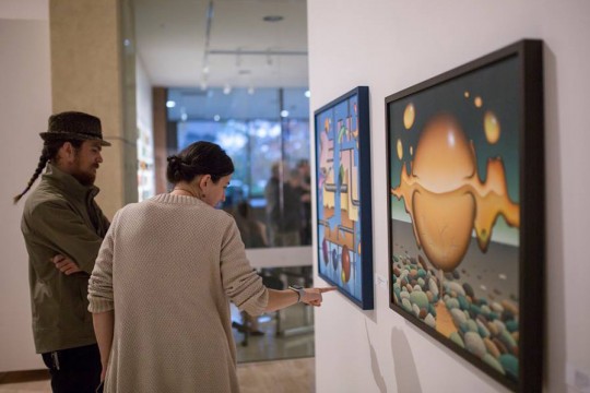 Two artists, a man and a woman, admire artwork on the wall of the gallery.