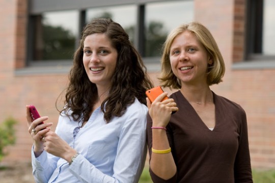 Two people posing for camera holding phones