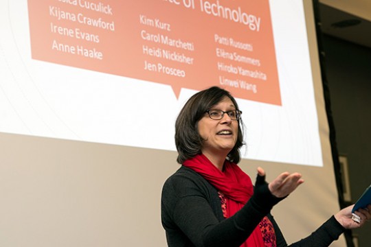 Person with red scarf presenting in front of screen.