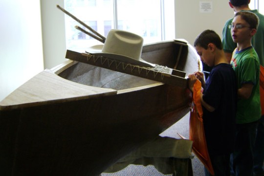 children looking at a wooden canoe.