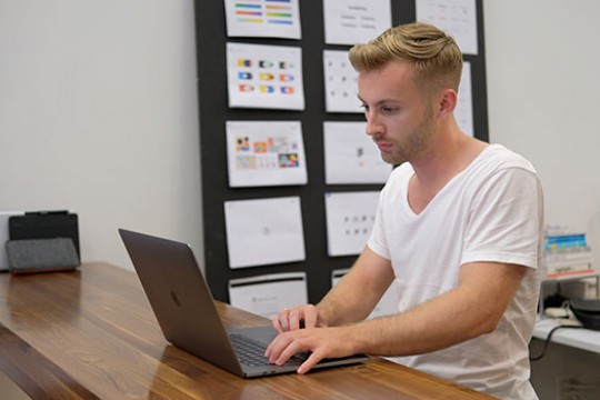 A photo of Cole Johnson standing at a high-top desk and working on his laptop.