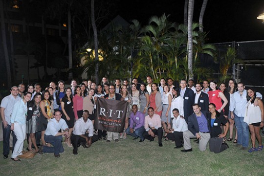 large group of people posing outside at night with an R I T banner.