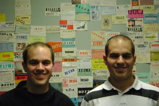 Two Students standing in front of board with amateur radio operator call signs.