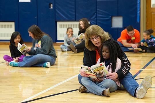 Adults reading to kids in a gym.