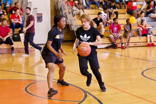 Two people playing basketball with people in the bleachers.