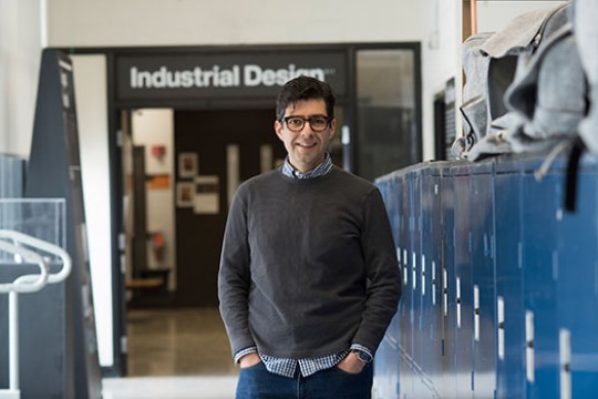 Alex Lobos standing next to lockers under a sign that says "Industrial Design".