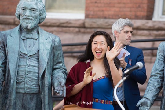 person waving next to her statue of Frederick Douglass.