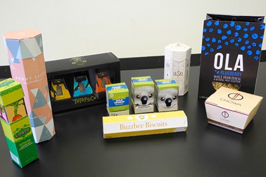 All of the student designed packaging laid out across a black table to showcase their designs.