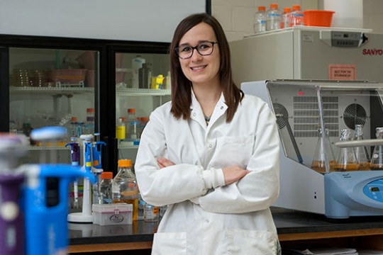 Nicole Pannullo in a white lab coat standing in a lab.