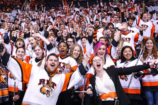 RIT pep band in matching RIT Jerseys pose for picture at hockey game.