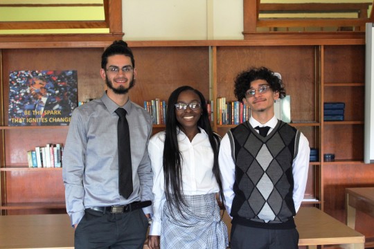 Three students pose for photo in front of book shelf.