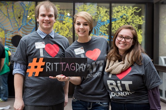 Three people Posing with "RIT Tag Day" sign