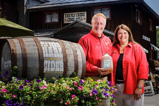 Bill and Brenda Michaels pose next to the entrance of their Cider Mill, holding a jug of their cider.