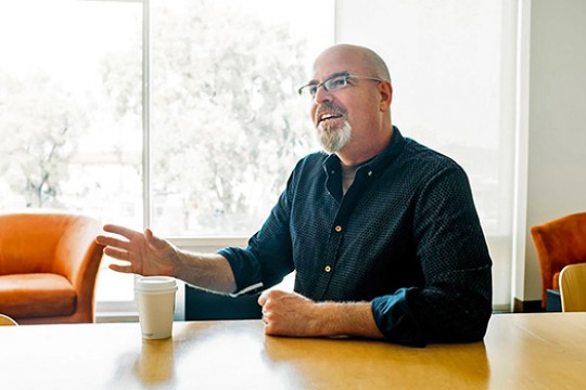John Butler sitting at a table with a cup of coffee.