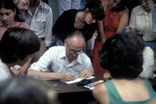 Person signing document at crowded table