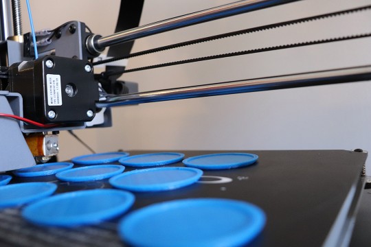 A 3D printer at work, printing 10 blue, flat, circular objects.