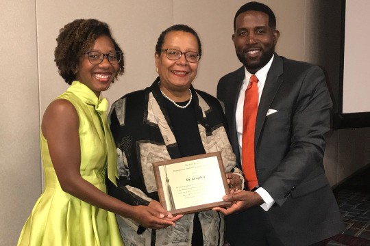 Three people pose for a photo holding dt ogilvie's, center, plaque she received for the Trailblazer Award.