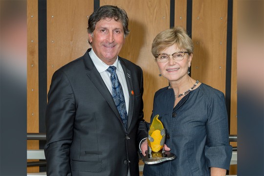 Steve Wear and Sophia Maggelakis pose for a photo together, Wear holding the distinguished alumni award trophy.