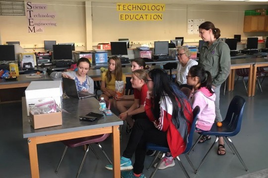 Group of middle-school students sits around a laptop computer.