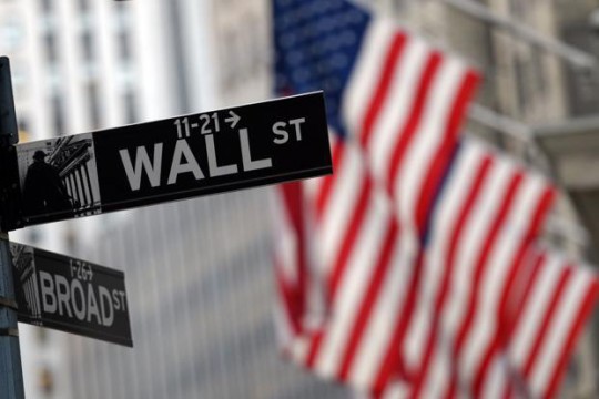 Street signs for Wall Street and Broad Street in foreground with American flags in the background