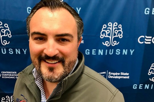Head-and-shoulders view of man posing in front of blue banner
