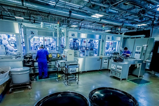 Workers stand at large robotic assembly line for disassembling iPhones.