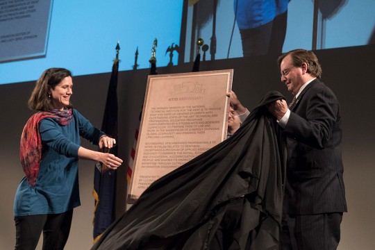 Two people pull cloak off of plaque.