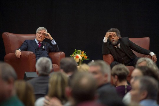 Two men in suits sit in arm chairs listening to audience members' questions.