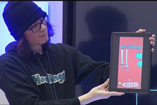 Student holds up iPad displaying a video game.