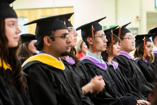 Students sitting, wearing graduation caps and gowns.