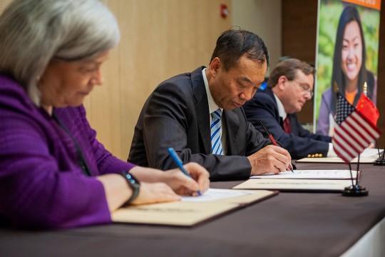 Three people sit at table signing papers.