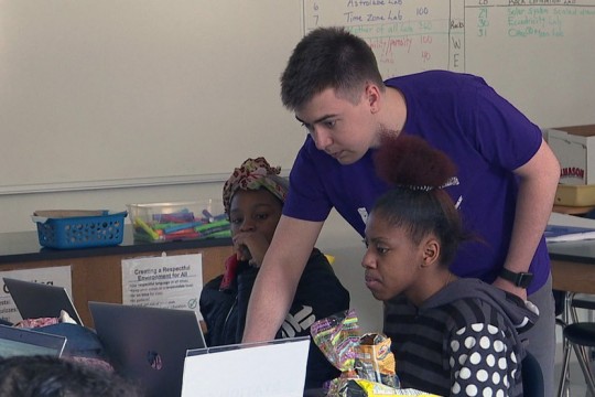 College student helps high school students on computer.