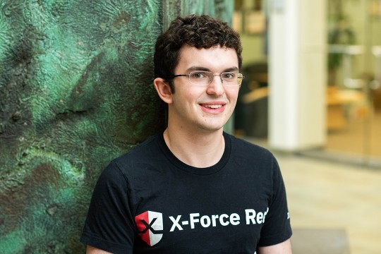 Student poses in front of green wall.
